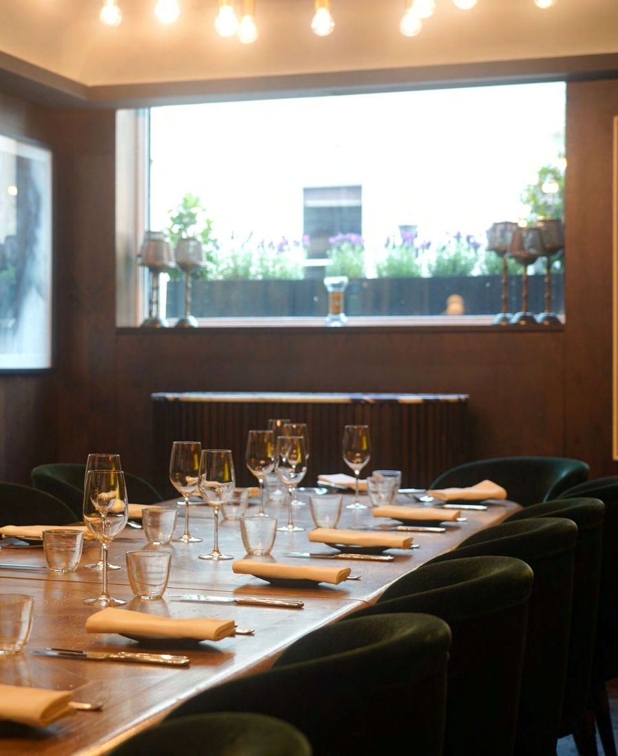 Event space dining table with wine glasses, green velvet chairs, golden pendant lights and garden terrace views