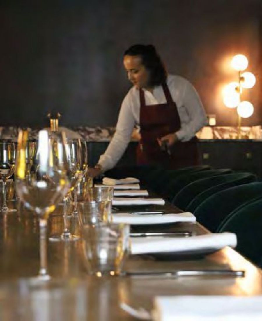 Event staff preparing elegant table with wine glasses and green velvet chairs in atmospheric lighting