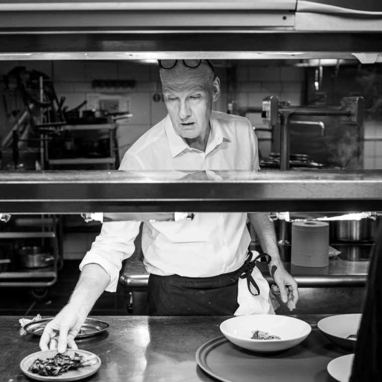 Chef Anthony Demetre plating dishes in professional kitchen black and white photograph