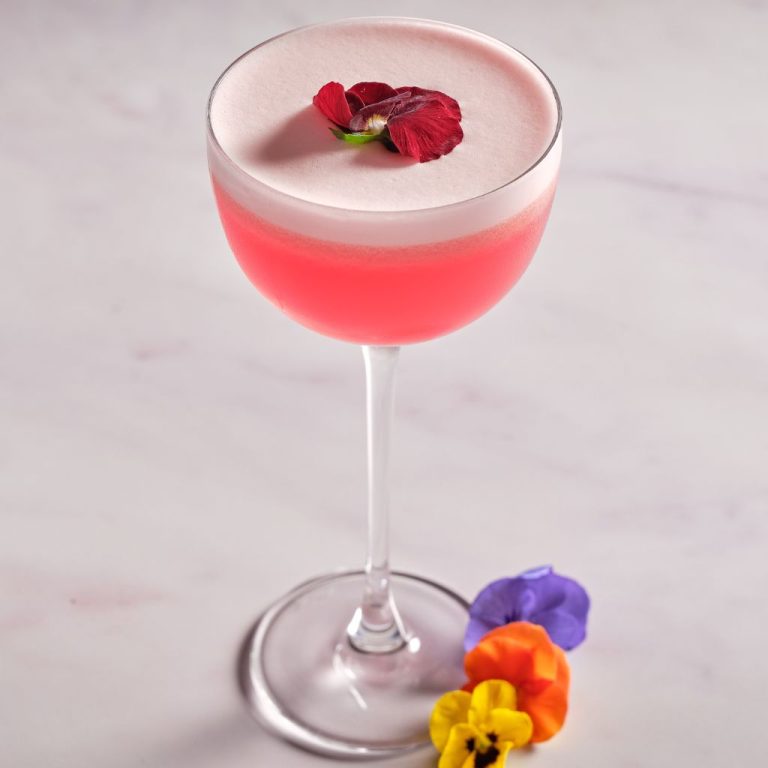 Elegant pink cocktail with foam top garnished with red flower and edible flowers