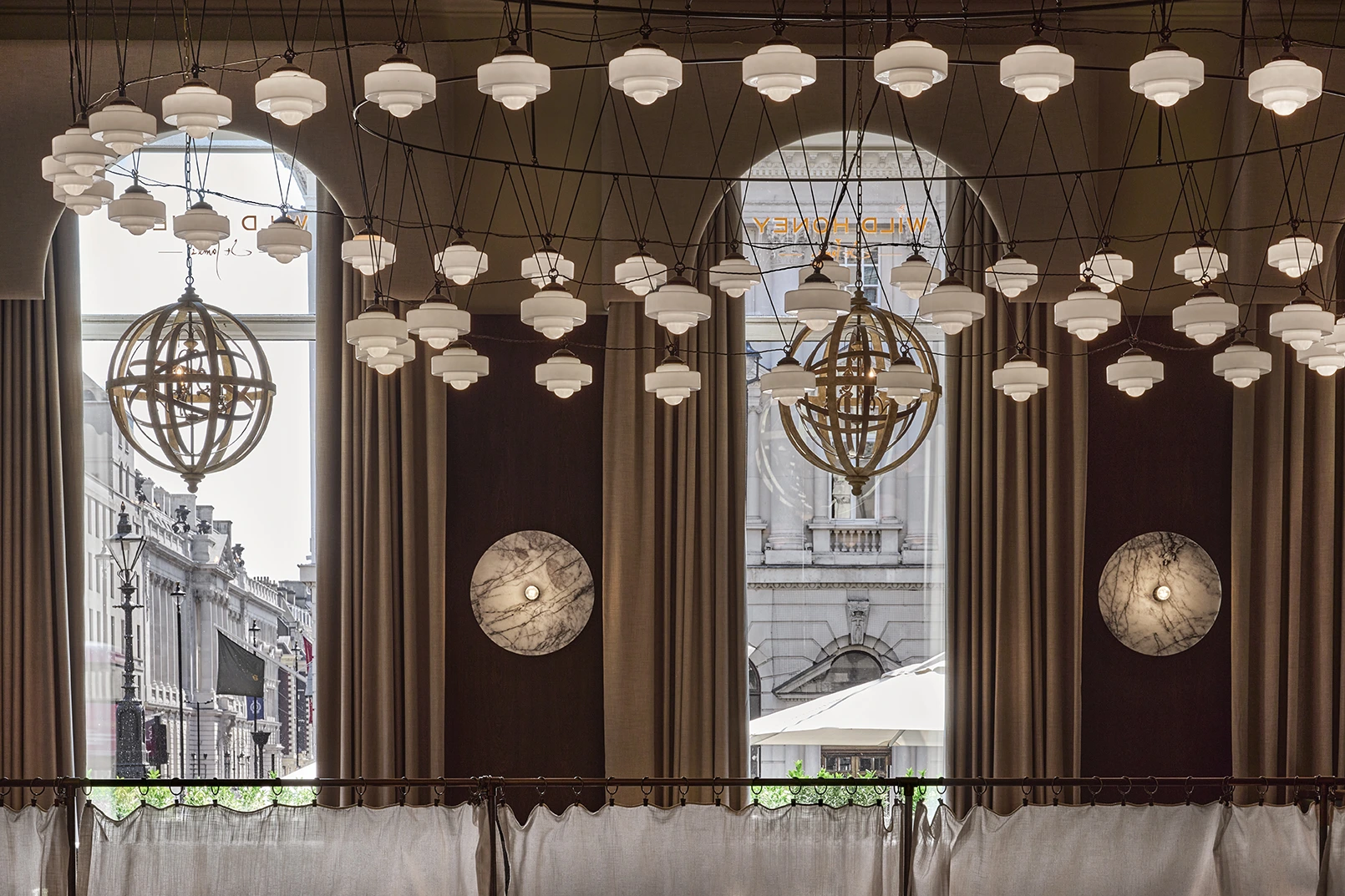 Wild Honey St James philosophy dining space with geometric sphere chandeliers, hexagonal pendant lights, large windows and London architecture views