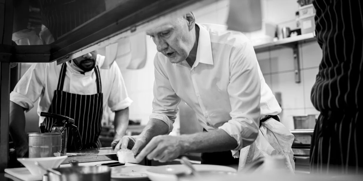Chef Anthony Demetre plating dishes in Wild Honey kitchen black and white